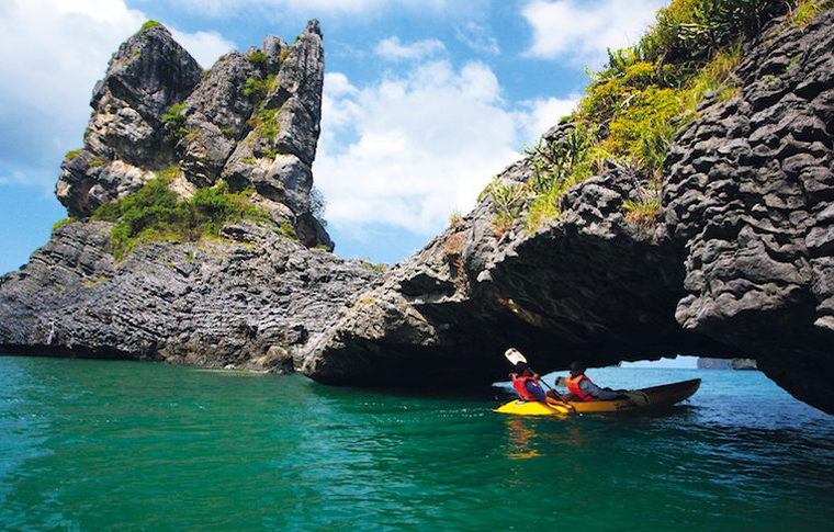 Kayakers paddling near the shore of a jagged rock island