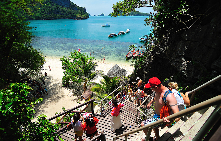 Group of people walking down a wooden walkway to a secluded white sand beach